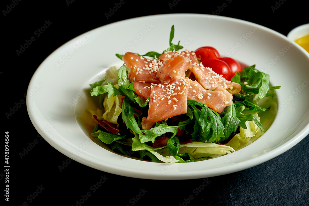 Diet salad with tomatoes and salmon in a white plate on a black background Diet salad with tomatoes and salmon in a white plate on a black background