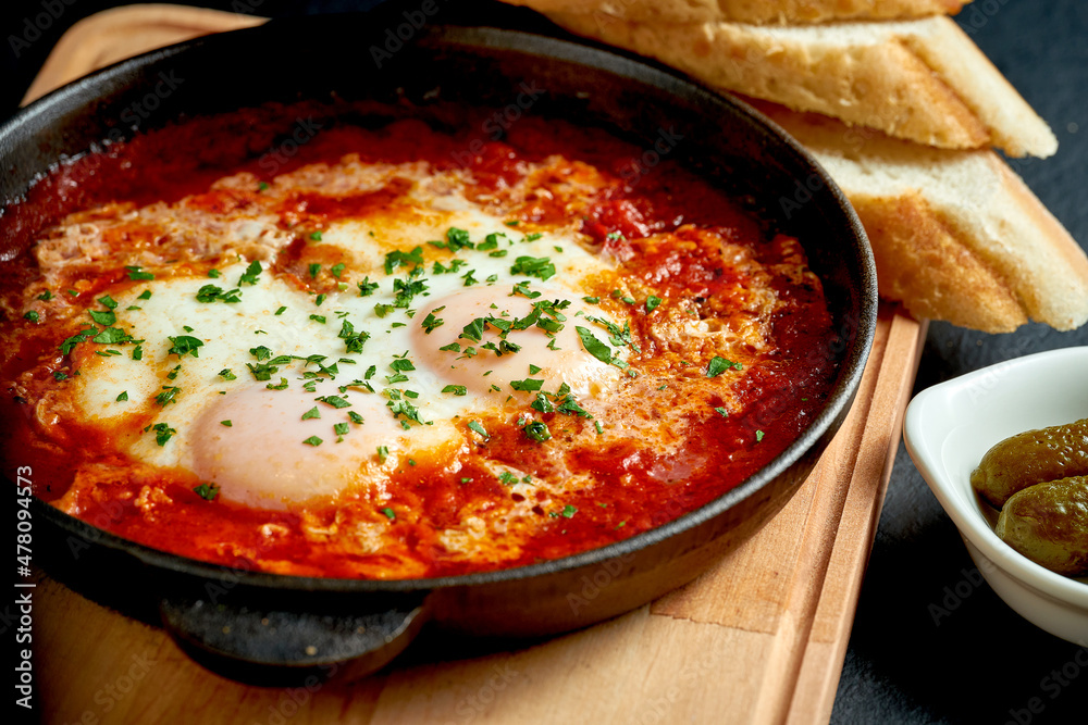Fried eggs shakshuka in tomato sauce in a frying pan on a white plate on a black background Fried eggs shakshuka in tomato sauce in a frying pan on a white plate on a black background