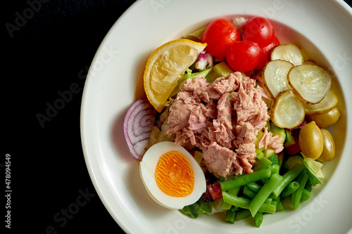 Diet nicoise salad with tuna, egg and asparagus in a white plate on a black background