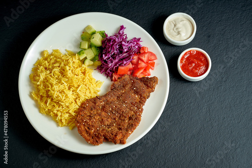 Chicken austrian schnitzel with rice and vegetables in a white plate on a black background