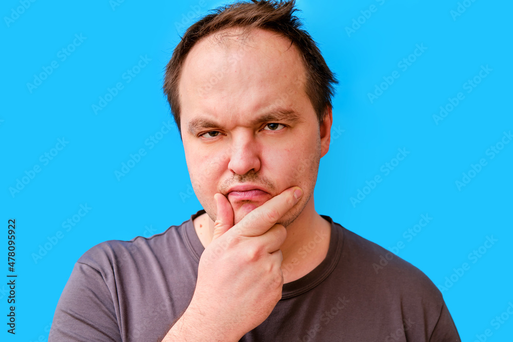 Portrait of a thoughtful adult man with a disheveled appearance, blue studio background