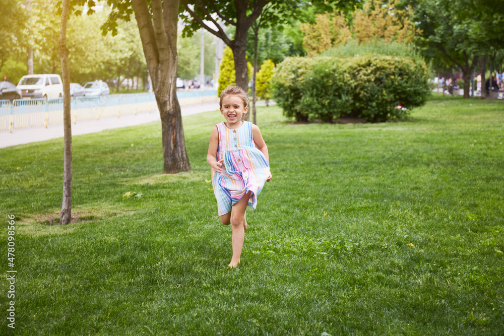 Happy girl running by grass while in colourful dress. Playing in park. Enjoying summer Happy girl running by grass while in colourful dress. Playing in park. Enjoying summer