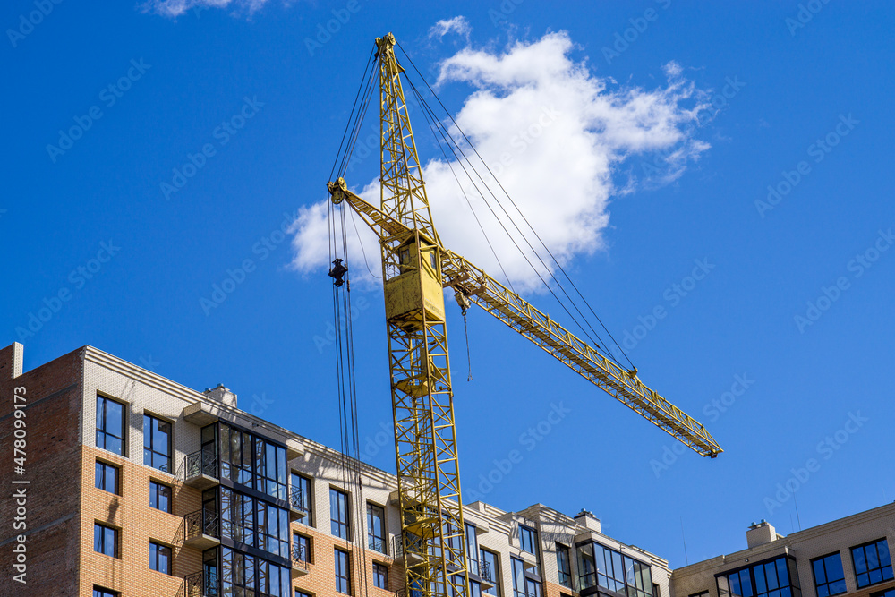 A tall construction tower crane against the sky and a building under construction.
