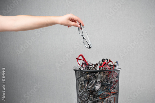Woman throws out unnecessary glasses for eyesight on pile in rubbish bin against grey background as request to improve poor vision macro