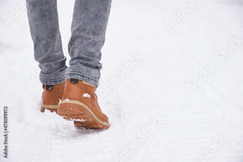 legs of a man in jeans and leather brown boots walking on a snowy road