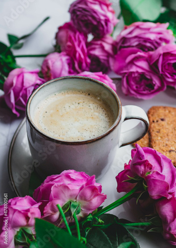 A mug of coffee with milk surrounded by roses. A morning gift and a good mood for a woman