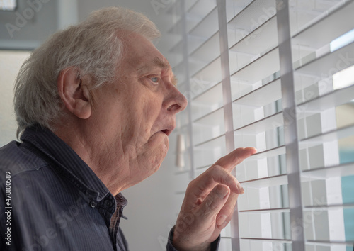 Senior man with funny facial expression looking out of window blinds 