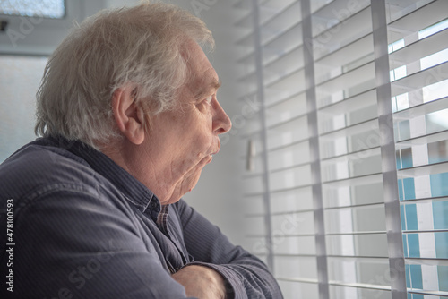 Senior man with shocked facial expression looking out of window blinds 