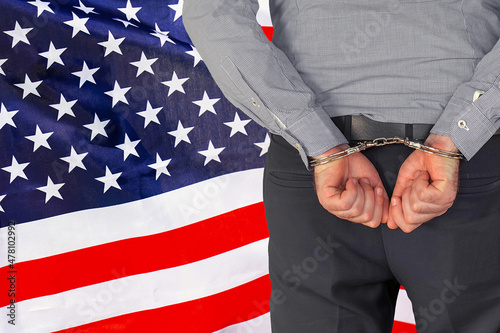Male with handcuffs on the background of the USA flag. Back view. Concept of prisons and corruption in US