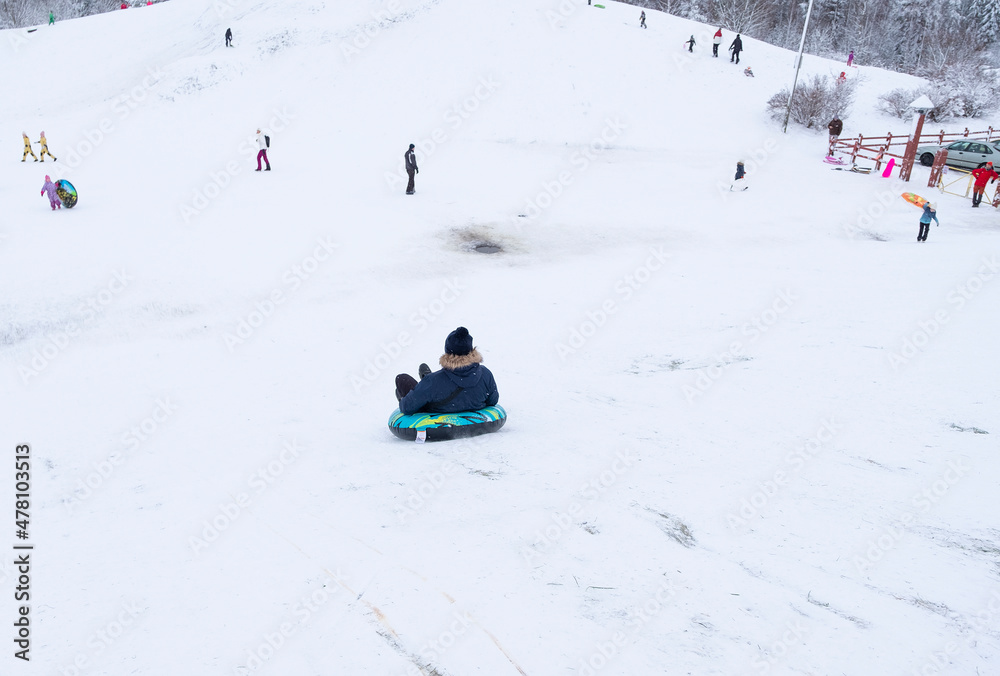 The man is having fun, riding down a snow-covered slide on an inflatable ring. Winter activities and recreation in Finland.