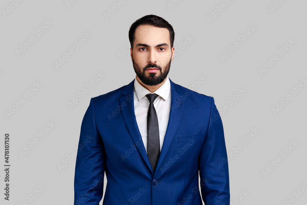 Self confident bearded male looking at camera with serious expression, unsmiling determined business man, wearing official style suit. Indoor studio shot isolated on gray background. Self confident bearded male looking at camera with serious expression, unsmiling determined business man, wearing official style suit. Indoor studio shot isolated on gray background.