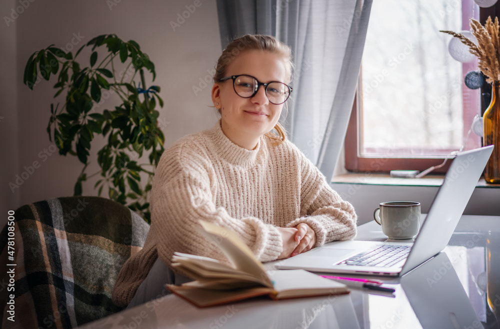 Happy young woman wearing glasses sitting at home and using laptop, online work and education concept Happy young woman wearing glasses sitting at home and using laptop, online work and education concept
