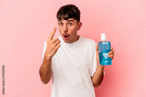 Young mixed race man holding mouthwash isolated on pink background having an idea, inspiration concept.