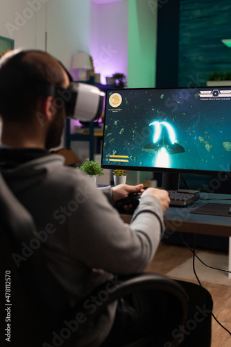 Person using vr goggles and joystick to play video games. Man with virtual reality headset holding controller in front of computer, playing online game. Player having fun with games.