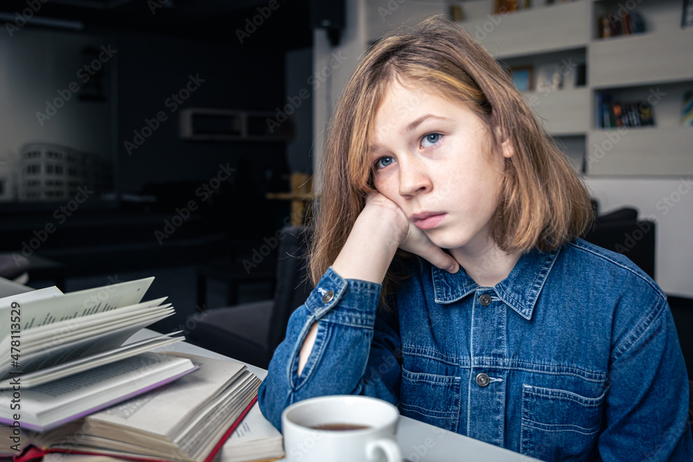 Tired girl in front of a laptop with a cup of tea and books. Tired girl in front of a laptop with a cup of tea and books.
