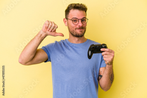 Young caucasian man holding a game controller isolated on yellow background feels proud and self confident, example to follow.