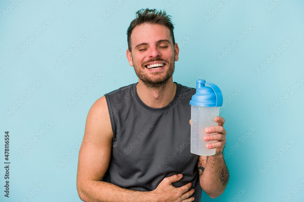 Young caucasian man drinking milkshake isolated on blue background laughing and having fun. Young caucasian man drinking milkshake isolated on blue background laughing and having fun.