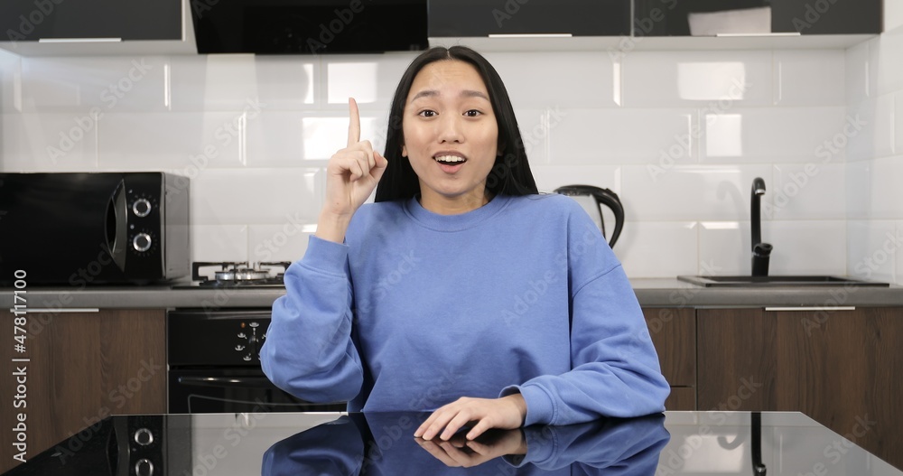 Attractive Asian woman is surprised at the camera. Woman model is sitting at the table in the kitchen. Attractive Asian woman is surprised at the camera. Woman model is sitting at the table in the kitchen.