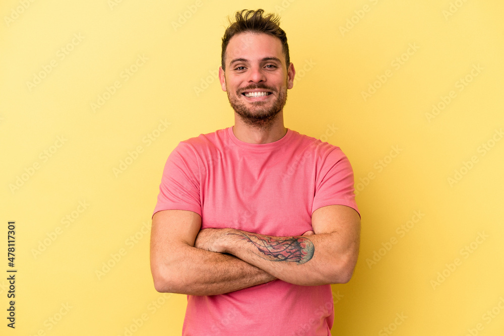 Young caucasian man isolated on yellow background who feels confident, crossing arms with determination.