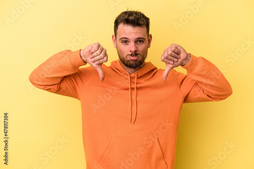 Young caucasian man isolated on yellow background showing a dislike gesture, thumbs down. Disagreement concept.