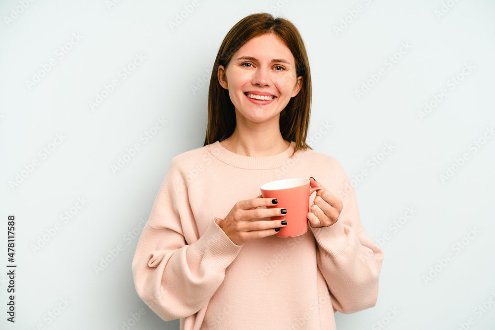 Young English woman holding a mug isolated on blue background happy, smiling and cheerful. Young English woman holding a mug isolated on blue background happy, smiling and cheerful.