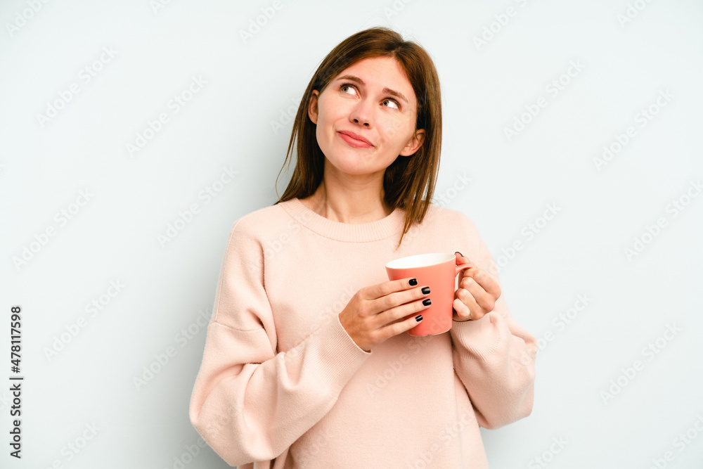 Young English woman holding a mug isolated on blue background dreaming of achieving goals and purposes Young English woman holding a mug isolated on blue background dreaming of achieving goals and purposes