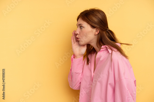 Young English woman isolated on yellow background is saying a secret hot braking news and looking aside © Asier