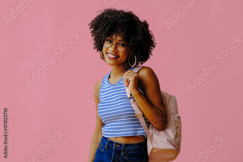 attractive girl in eyeglasses with backpack posing on pink background, back to school college concept