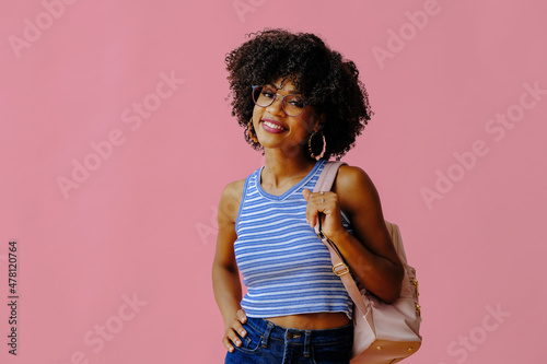 beautiful smiling girl in eyeglasses with backpack posing on pink background, back to school concept