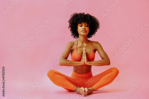 beautiful African american woman meditating in sports outfit on pink background photo