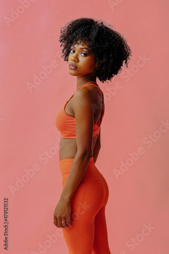 young fit african american woman in sports outfit posing isolated on pink background