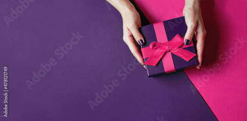 Women's hands with a beautiful manicure hold a gift with a pink bow on a purple background. photo