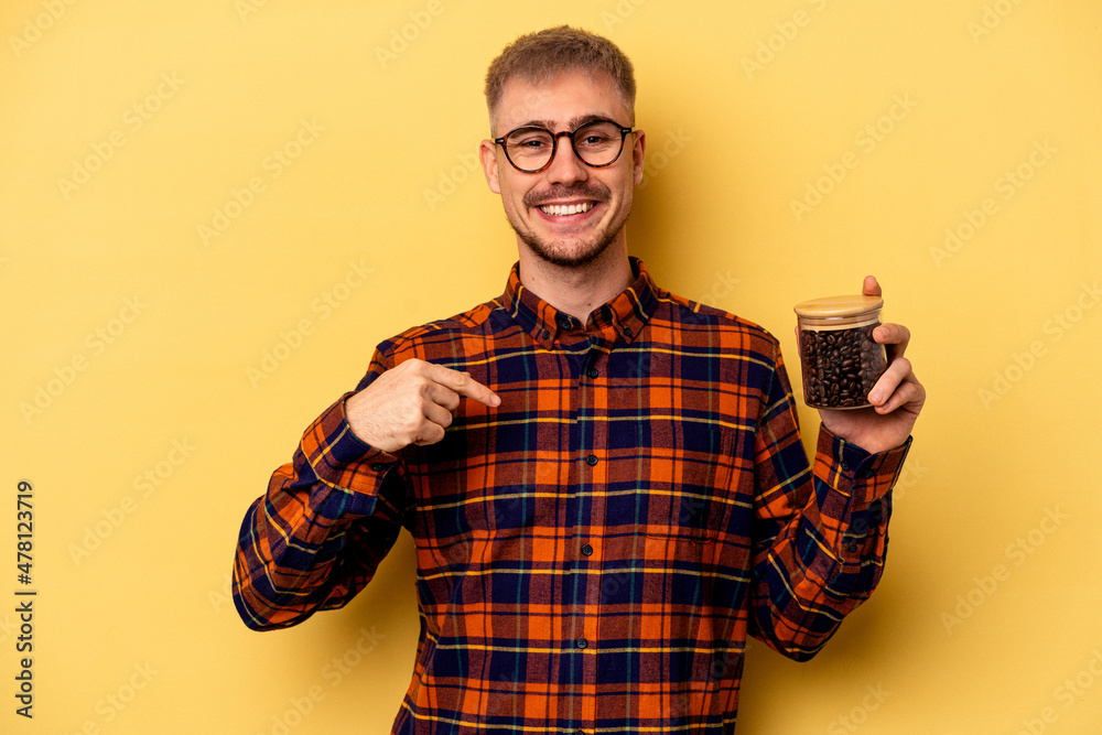 Young caucasian man holding coffee jar isolated on yellow background person pointing by hand to a shirt copy space, proud and confident Young caucasian man holding coffee jar isolated on yellow background person pointing by hand to a shirt copy space, proud and confident