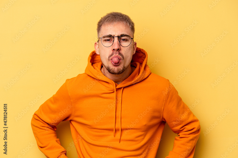 Young caucasian man isolated on yellow background funny and friendly sticking out tongue. Young caucasian man isolated on yellow background funny and friendly sticking out tongue.