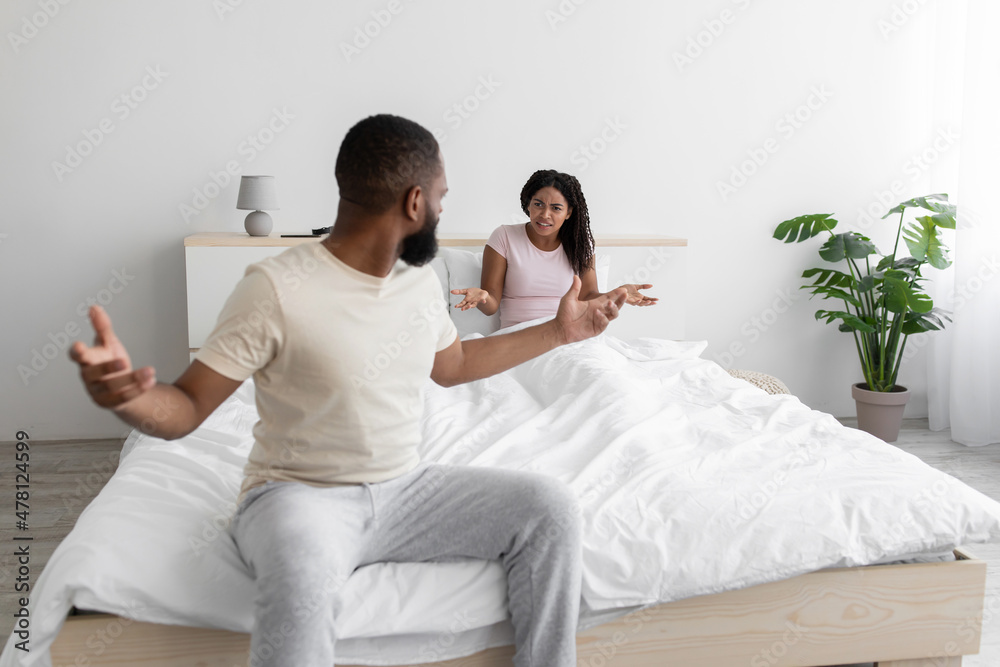Irate unhappy excited millennial black woman and man swearing, freaking out, shouting and gesturing on bed