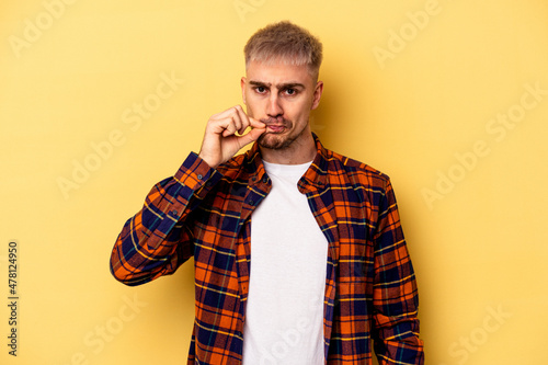 Young caucasian man isolated on yellow background with fingers on lips keeping a secret. © Asier
