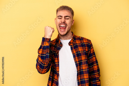 Young caucasian man isolated on yellow background celebrating a victory, passion and enthusiasm, happy expression. © Asier