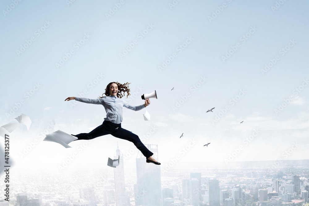 Portrait of energetic businesswoman with megaphone jumping in open air