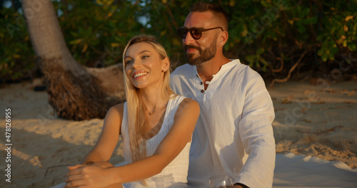 Young blonde woman and man in white shirt dating on evening beach during sun set