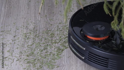 A robot vacuum cleaner removes the fallen needles from the Christmas tree. Technologies that help housewives clean the apartment. Close-up of a vacuum cleaner moving across the floor.