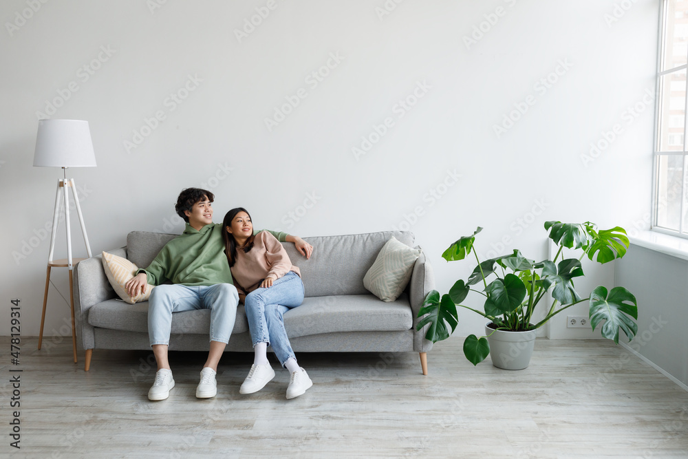 Spending weekend together. Happy millennial Asian couple resting on couch at home, empty space Spending weekend together. Happy millennial Asian couple resting on couch at home, empty space