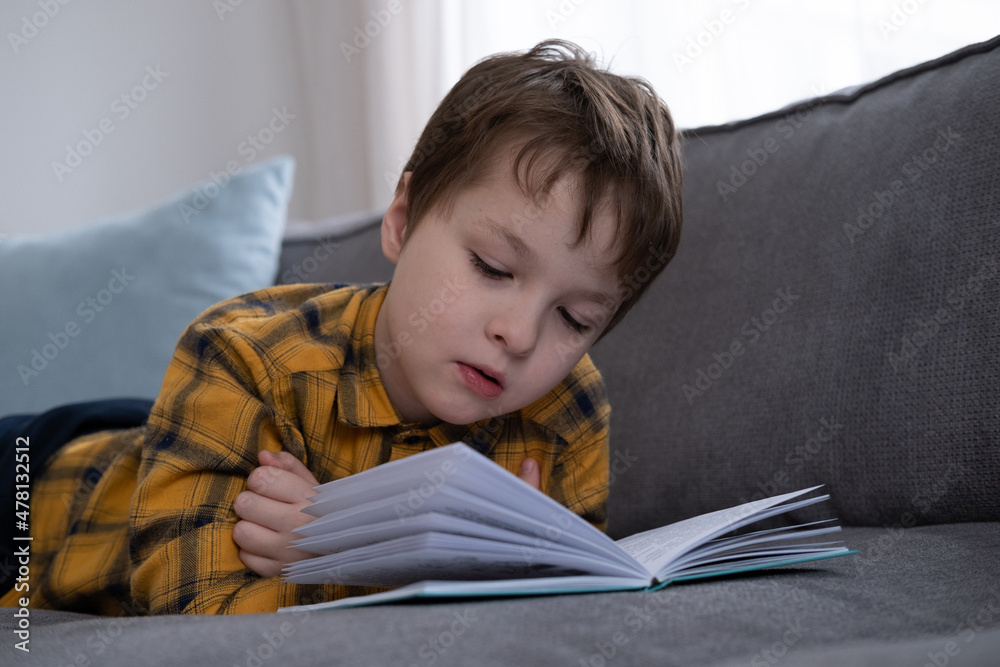 little boy lying on the sofa and reading a book little boy lying on the sofa and reading a book