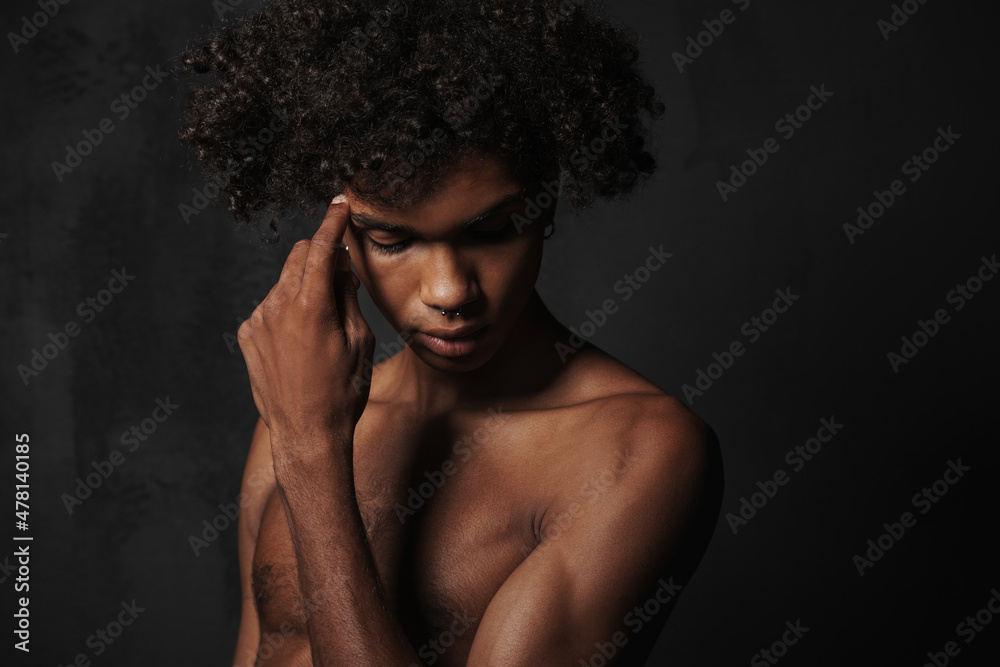Shirtless black man with piercing posing and looking downward Shirtless black man with piercing posing and looking downward