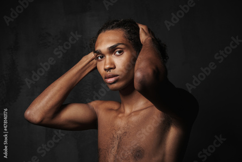 Shirtless black man with piercing holding his head and looking at camera