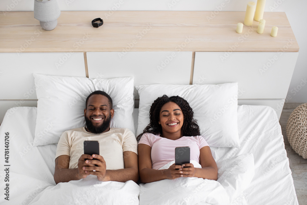 Smiling young african american husband and wife typing on phones ...