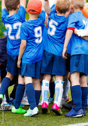 Vertical picture of happy boys in sports team celebrating success together. School kids in blue sporty jersey shirts with white numbers. Children playing sports on grass venue