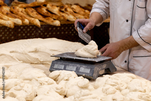 Baker weighing dough portions for baking buns at the manufacturing. Man weighing raw dough on scale in bakery.