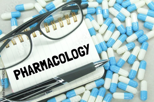 glasses, pens, blue and white pill notebooks scattered with the word pharmacology photo