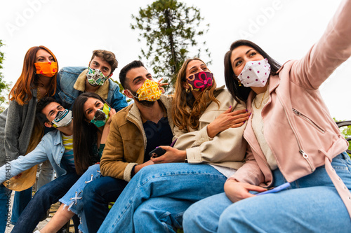 Selfie of young smiling people having fun together wearing face mask - Happy friends group taking selfie in park at european trip - Young people addicted by sharing stories on social network community