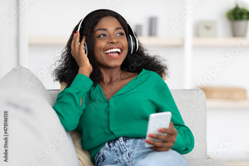 Positive black woman with wireless headset and smartphone at home